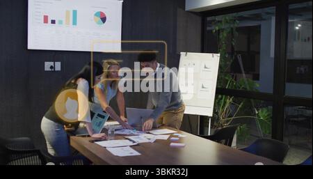 Examinez l'équipe penchée au-dessus de la table examinez les tableaux au bureau, avec un ordinateur portable, des notes adhésives et des stylos Banque D'Images