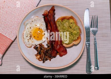 Copieux petit déjeuner avec bacon croustillant, œuf au plat, champignons sautés et pain grillé crémeux à l'avocat sur un plat rustique en céramique, parfait pour les menus du brunch. Banque D'Images