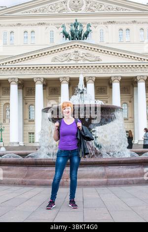 moscou, russie, 14.06.2017 Une femme en chemise violette se tient devant une fontaine. Elle sourit et tient un sac à dos. La scène se déroule devant o Banque D'Images