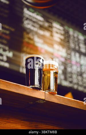 Deux verres à bière avec des sélections de bière artisanale sur le comptoir du bar avec fond flou présentant des options de boisson Banque D'Images