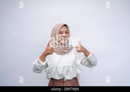 Portrait femme indonésienne heureuse portant le hijab montre le pouce vers le haut et regardant la caméra sur fond blanc. Banque D'Images
