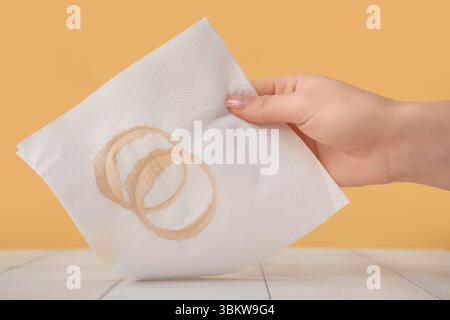 Femme essuyant le café renversé avec une serviette en papier sur la table de tuiles blanches près du mur jaune Banque D'Images