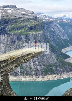 Un aventurier solitaire se dresse en toute confiance au bord de la randonnée Trolltunga en Norvège, surplombant le serein Lysefjord. Banque D'Images