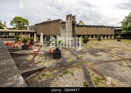L'espace extérieur du musée Sainte-Croix à Poitiers (Vienne, Nouvelle-Aquitaine, France), avec un parvis pavé, des sièges de café et des palmiers en jardinières noires. Le bâtiment du musée brutaliste, datant du début des années 1970, contraste avec les bâtiments résidentiels historiques des environs. Le musée borde le site archéologique de l'ancienne Poitiers (Limonum). En 1974, le Musée Sainte-Croix a reçu un prix pour son architecture brutaliste, caractérisée par l’utilisation de béton apparent, des lignes épurées et des formes géométriques simples. Rue Saint Simplicien, Poitiers, Nouv Banque D'Images