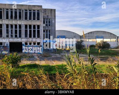 Complexe industriel délabré avec graffitis et végétation envahie, symbolisant la décomposition urbaine et l'abandon Banque D'Images