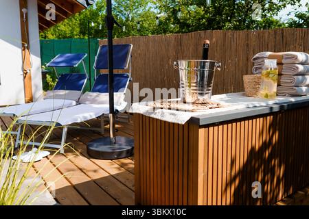 Une photo de style de vie paisible en plein air comprend deux confortables chaises longues bleues, un bain à remous, une bouteille de champagne rafraîchissant dans un seau à glace et une serviette roulée Banque D'Images