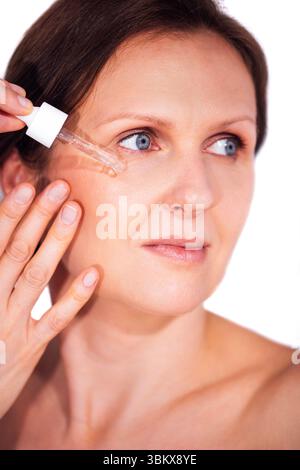 Une femme d'âge moyen applique doucement le sérum sur son visage. Une dame tient une pipette avec une essence hydratante et coule sur la peau près de son œil. Voiture Banque D'Images