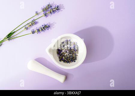 Mortier et pilon avec des fleurs de lavande séchées sur fond violet avec lumière et ombres. Phytothérapie naturelle, concept d'aromathérapie. Vue de dessus Banque D'Images