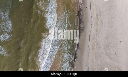 Les vagues vibrantes roulent doucement sur la plage de sable doux du Danemark, créant une atmosphère tranquille. Un personnage solitaire se promène le long du bord de l'eau, immergé dans la beauté de la nature. Banque D'Images