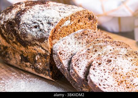 Le pain de seigle fraîchement cuit repose sur une surface en bois avec des tranches coupées, mettant en valeur sa texture et son arôme invitant dans une atmosphère chaleureuse de cuisine. Banque D'Images