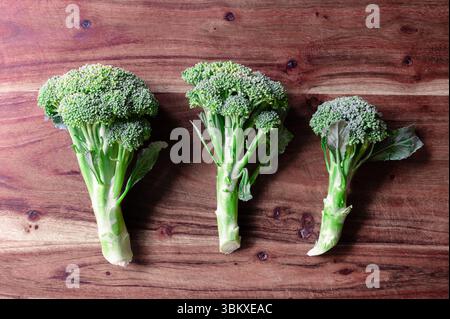 Trois têtes de brocoli alignées sur une planche à découper en bois Banque D'Images