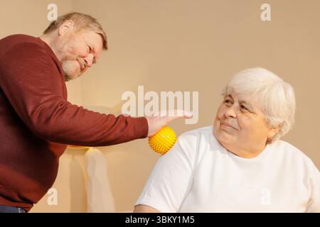 Couple de personnes âgées utilisant une boule de thérapie de massage spiky pour soulager la douleur à l'épaule récupération musculaire et soutien de bien-être à la maison Banque D'Images