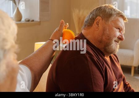 Couple de personnes âgées utilisant une boule de thérapie de massage spiky pour soulager le mal de dos récupération musculaire et soutien de bien-être à la maison Banque D'Images
