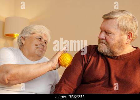 Couple de personnes âgées utilisant une boule de thérapie de massage spiky pour soulager le mal de dos récupération musculaire et soutien de bien-être à la maison Banque D'Images
