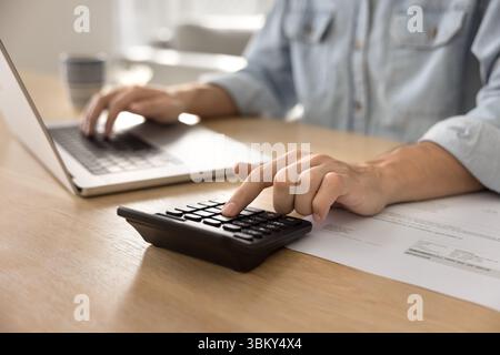 Gros plan recadré des mains d'homme d'affaires à l'aide d'un ordinateur portable et d'une calculatrice Banque D'Images