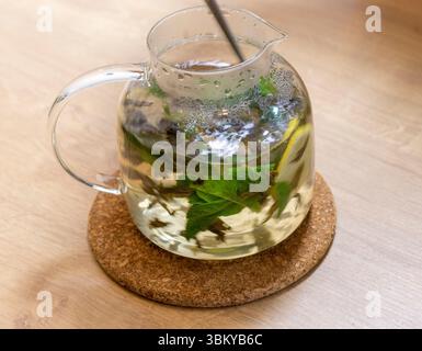 Théière transparente élégante avec des feuilles de thé vert juste infusées, des feuilles de menthe et des tranches de citron dedans Banque D'Images