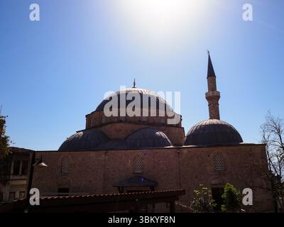 Une photo sous-angle capture la grandeur architecturale d'une mosquée, mettant en valeur ses dômes et son minaret dans un ciel bleu clair, soulignant son importance culturelle et religieuse. Banque D'Images