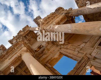 Une photo sous-angle capture l'architecture complexe de la Bibliothèque de Celsus à Éphèse, en Turquie, mettant en valeur ses colonnes imposantes et ses sculptures ornées sur fond d'un ciel partiellement nuageux, soulignant l'importance historique et la grandeur architecturale de cette ancienne structure romaine. Banque D'Images