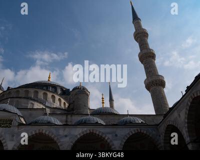Une photo sous-angle capture la grandeur architecturale de la Mosquée bleue d'Istanbul, en Turquie, mettant en valeur ses dômes, ses minarets et ses détails complexes sur fond de ciel partiellement nuageux. Banque D'Images