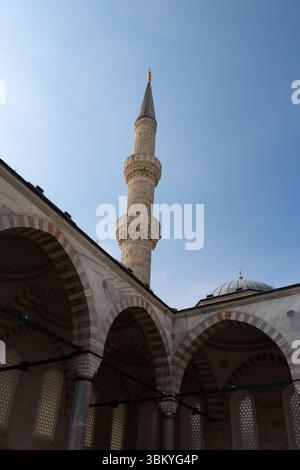 Une prise de vue en angle bas capture les détails architecturaux d'une mosquée, mettant en valeur son minaret, ses arches et son dôme contre un ciel bleu clair. Banque D'Images