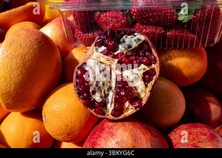 Un gros plan présente un assortiment vibrant de fruits, y compris des oranges, des grenades et un contenant de fraises, créant un affichage coloré et appétissant. Banque D'Images