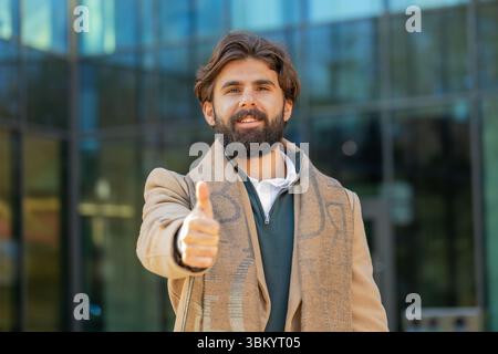 J'aime. Homme d'affaires heureux soulève le pouce vers le haut est d'accord avec quelque chose ou donne une réponse positive recommande la publicité aime la rétroaction de bonne idée, célébrant la victoire de succès. Guy debout sur la rue urbaine de la ville Banque D'Images