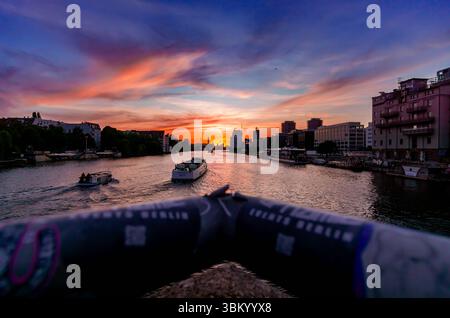 Coucher de soleil doré sur la rivière Spree de Berlin, vue depuis le pont Oberbaum avec des bateaux qui traversent des silhouettes urbaines. Banque D'Images