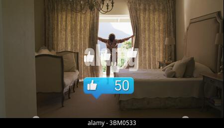 Tirant vers l'arrière rideaux floraux femme senior dans la robe florale à la fenêtre dans la chambre, montrant la vue du balcon Banque D'Images