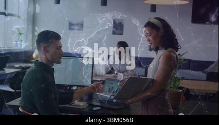 Discuter avec des collègues tenant un ordinateur portable et tapant dans un bureau ouvert, avec une superposition de carte du monde numérique Banque D'Images