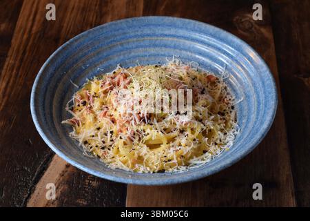 Bol bleu avec pâtes carbonara saupoudrées de parmesan Banque D'Images