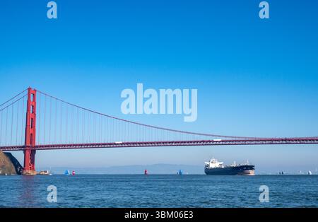 Un grand cargo navigue sous le Golden Gate Bridge, tandis que des voiliers sont également sur l'eau. Banque D'Images