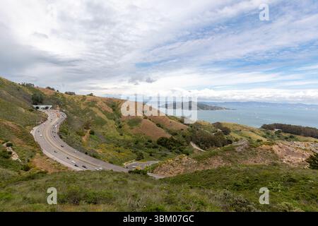Une vue panoramique d'une autoroute serpentant à travers des collines, avec des voitures voyageant le long de la route, et un plan d'eau avec une île au loin. Banque D'Images