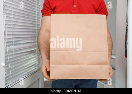 Courrier masculin avec sac en papier à la porte. Service de livraison de nourriture Banque D'Images
