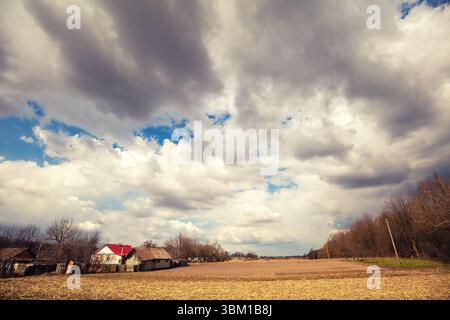 Vue d'un champ labouré à la périphérie d'un village par une journée partiellement nuageuse. Paysage rural au début du printemps Banque D'Images