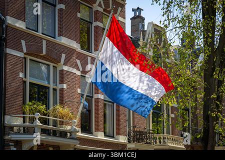 Un drapeau hollandais vibrant bat contre un bâtiment traditionnel en briques aux pays-Bas, incarnant la fierté nationale par une journée ensoleillée le jour du Roi ou Libera Banque D'Images
