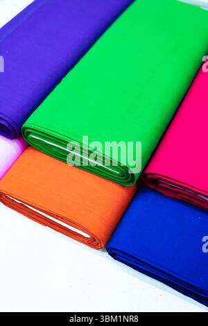 Vue rapprochée de plusieurs rouleaux de tissu coloré dans différentes nuances, y compris violet, vert, orange, rose, et bleu. Les tissus sont soigneusement disposés Banque D'Images