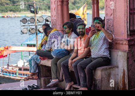 Inde, Jaipur, 22 mars 2025. Les hommes couverts de poudre Holi reposent près des marches du temple au bord du lac à Jaipur. Franc moment de célébration haute en couleur par le Wate Banque D'Images