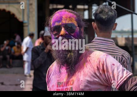 Inde, Jaipur, 22 mars 2025. Homme barbu couvert de poudre colorée pendant les célébrations du festival Holi à Jaipur. Portrait de rue avec lunettes de soleil Banque D'Images