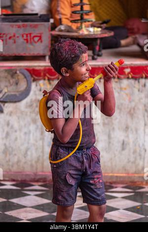 Inde, Jaipur, 22 mars 2025. Garçon souriant jouant avec un pistolet à eau pendant le festival Holi à Jaipur. Portrait franc de la joie de l'enfance au festival Banque D'Images