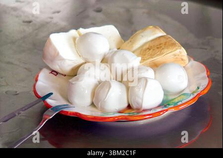 Petites boules de mozzarella fraîches. Un morceau de grande mozzarella et un morceau de fromage fumé sont disposés sur une assiette colorée. Prêt à être mangé. Avec un for Banque D'Images