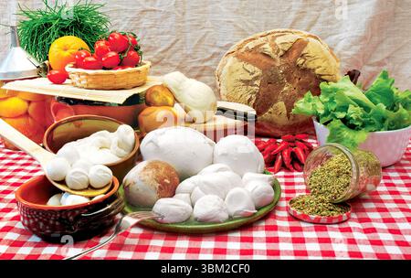 Disposer différentes tailles de fromages mozzarella sur une nappe à carreaux avec des légumes frais, du pain et des herbes crée un affichage vibrant de c italien Banque D'Images