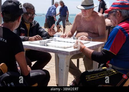 Hommes jouant aux dominos le long de la plage de nova icaria, Barcelone, Espagne. Banque D'Images
