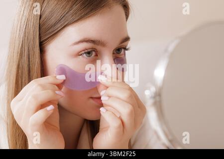 Gros plan de jeune femme appliquant de l'hydrogel sous les patchs oculaires pour le soin des rides de rajeunissement et la routine de beauté du visage Banque D'Images
