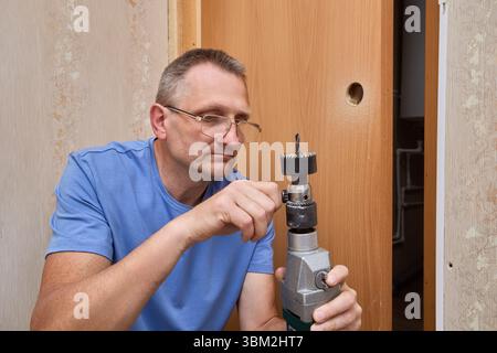 Le spécialiste de la scie cloche utilise une clé de mandrin pour desserrer le mandrin de perçage et libérer la scie cloche montée sur arbre après avoir percé le trou pour l'installation du verrou. Banque D'Images