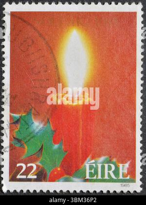 Timbre-poste annulé imprimé par l'Irlande, qui montre bougie allumée et houx, Noël, vers 1985. Banque D'Images