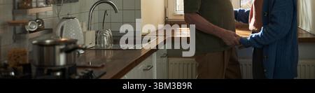 En-tête de couple senior embrassant dans la cuisine moderne, debout près de la fenêtre avec la lumière naturelle, montrant un moment affectueux, engagé dans une conversation amoureuse Banque D'Images