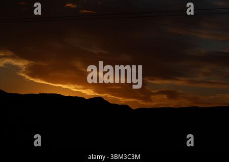 Coucher de soleil doré sur des silhouettes de montagne dans le Karoo, Afrique du Sud. Ciel nocturne spectaculaire avec des nuages chauds et un horizon rural paisible. Banque D'Images