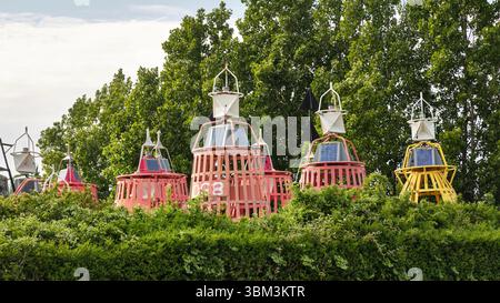 28 mai 2025 - Vlissingen-pays-Bas : rangée de bouées de navigation maritime colorées avec des panneaux solaires sur le dessus, partiellement visible au-dessus d'une haie verte au th Banque D'Images
