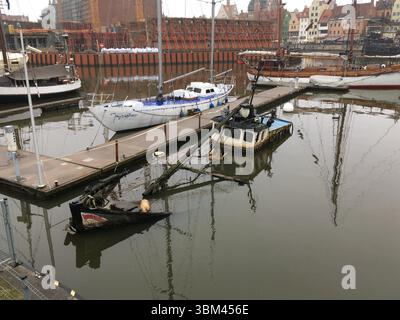 Un chalutier de pêche partiellement coulé se trouve dans la vieille marina de Gdańsk, sur la rivière Motława – les bois altérés évoquent la décomposition maritime et la nostalgie urbaine Banque D'Images