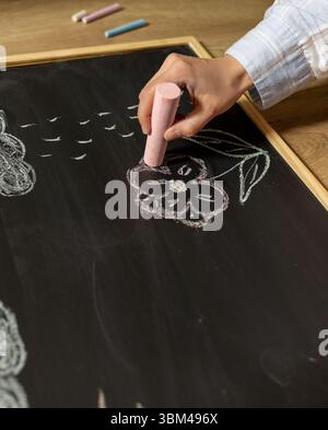 fille dessine la fleur et le soleil avec la craie colorée sur le tableau noir. dessin simple pour enfants sur tableau de craie noire Banque D'Images